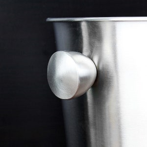 May include: Close-up of a silver ice bucket with a rounded handle. The handle is smooth and polished.