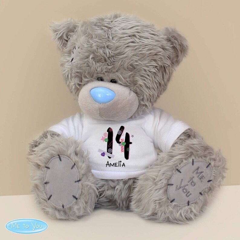 May include: Grey plush teddy bear wearing a white t-shirt with the number 14 decorated with colourful candy and the name Amelia. The bear has a blue nose and the words "Me to You" are printed on the bottom of the image.