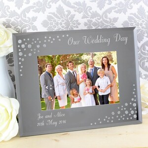 K&ouml;nnte beinhalten: Ein silberner Bilderrahmen mit wei&szlig;em Hintergrund und einem Foto einer Hochzeitsgesellschaft. Der Rahmen hat einen silbernen Glitzer-Rand und der Text "Our Wedding Day" und "Joe and Alice 20th May 2016" ist in den Rahmen graviert.