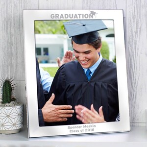Pu&ograve; includere: Cornice per foto argentata per la laurea con una foto in bianco e nero di una persona con un cappello e una toga da laurea. La cornice ha il testo "GRADUATION" e "Spencer Meakin Class of 2016".