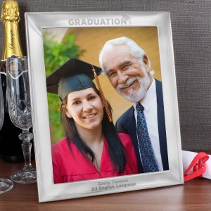 Pu&ograve; includere: Cornice per foto d'argento per la laurea con una foto di un laureato e un membro della sua famiglia. La cornice ha le parole "GRADUATION" incise in alto e il nome del laureato, il titolo di studio e l'anno di laurea incisi in basso.