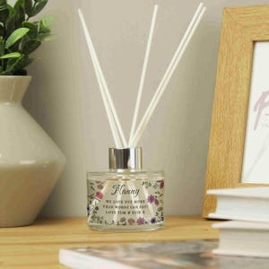 May include: A clear glass diffuser bottle with a silver lid and white diffuser sticks. The bottle has a floral design and the text "Nanny We love you more than words can say! Love Tom & Evie X".