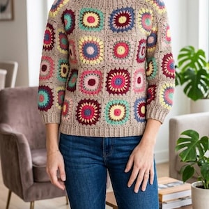 May include: A beige crochet sweater with colorful square patterns. The squares feature various colors including red, yellow, blue, and green. The sweater has a round neckline and three-quarter sleeves. The model is wearing blue jeans.