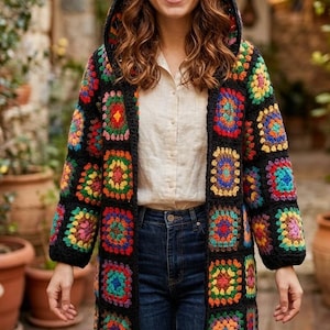 May include: A hooded, long-sleeved crochet cardigan in a patchwork design. The black cardigan features colorful squares in shades of red, orange, yellow, green, blue, and purple. The person is wearing a light-colored shirt and blue jeans.