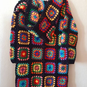 May include: A black crochet cardigan with a hood, featuring a colorful patchwork design of granny squares. The cardigan has a long, loose fit and a fringed hem.