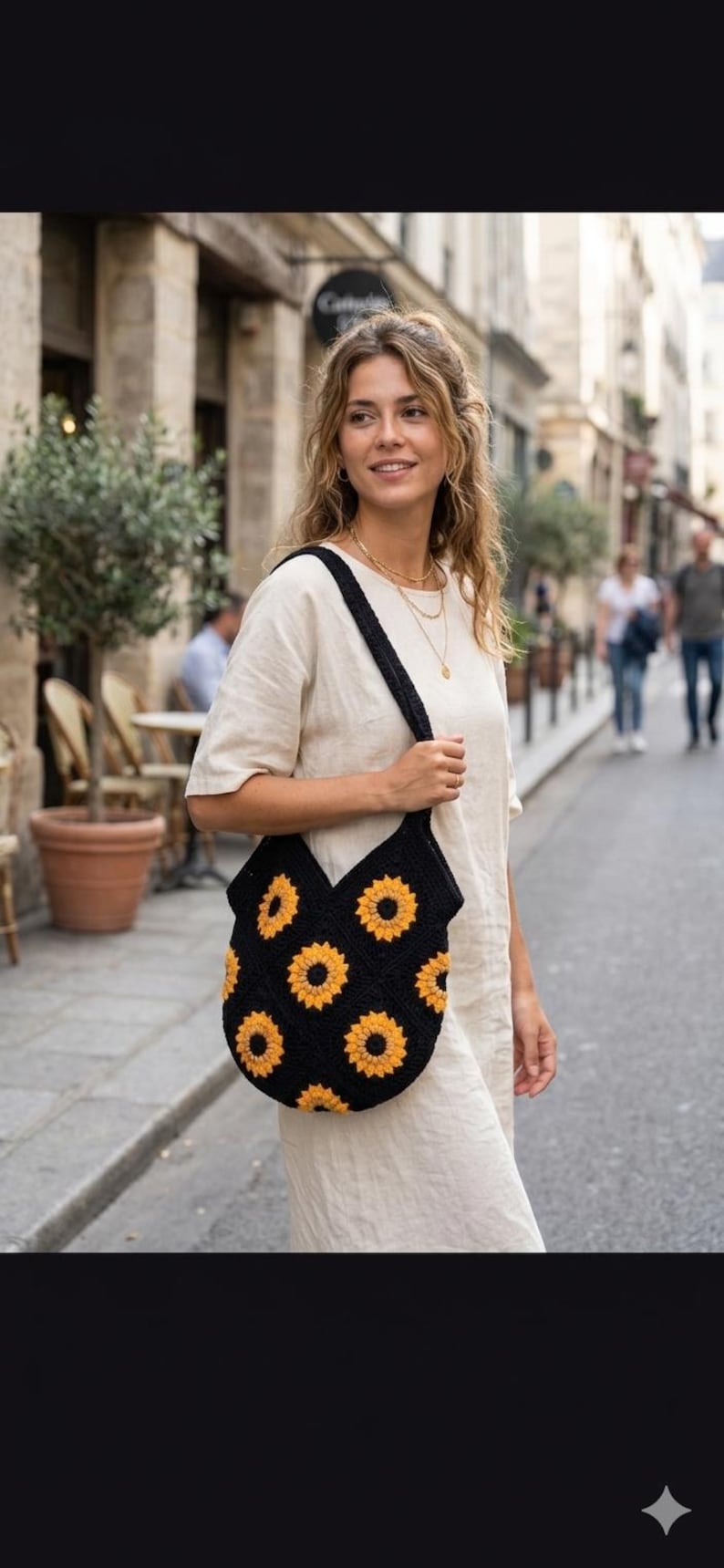 May include: Black crochet tote bag with a sunflower pattern in yellow and orange. The bag has a wide strap and is carried over the shoulder. The bag is made of a soft, textured material.