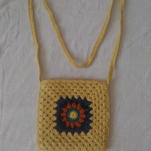 May include: A yellow crocheted crossbody bag with a colorful circular design in the center.