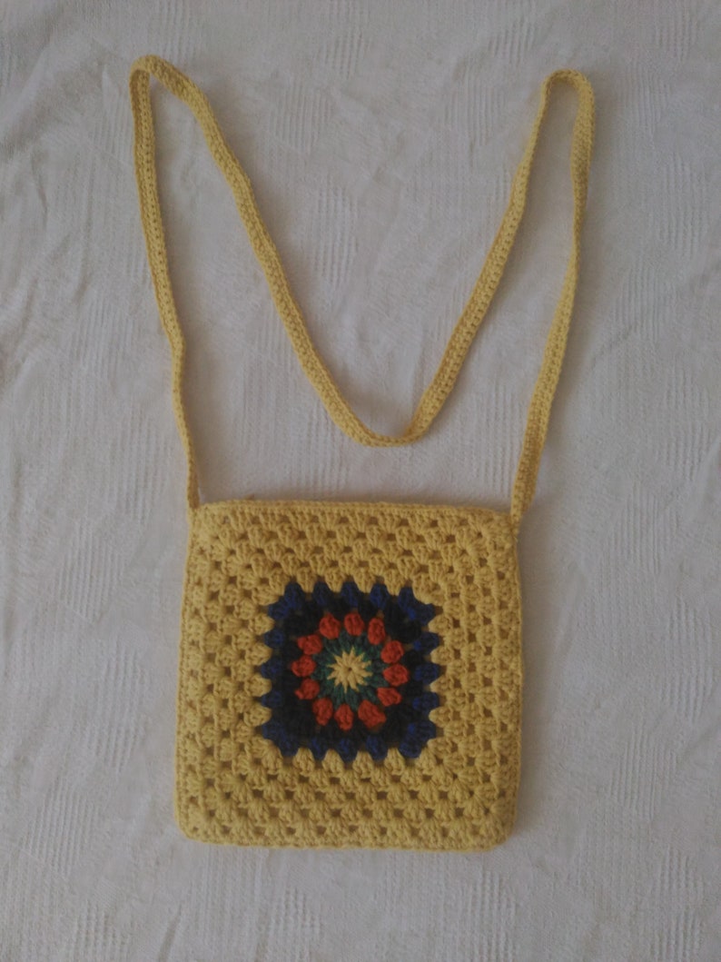 May include: A yellow crocheted crossbody bag with a colorful circular design in the center.