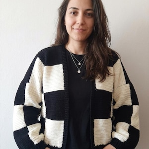 Puede incluir: Un cárdigan de crochet negro y crema con un patrón de tablero de ajedrez. El suéter tiene mangas largas y un ajuste relajado. La combinación de colores es una combinación clásica de negro y crema, creando un aspecto gráfico y audaz.