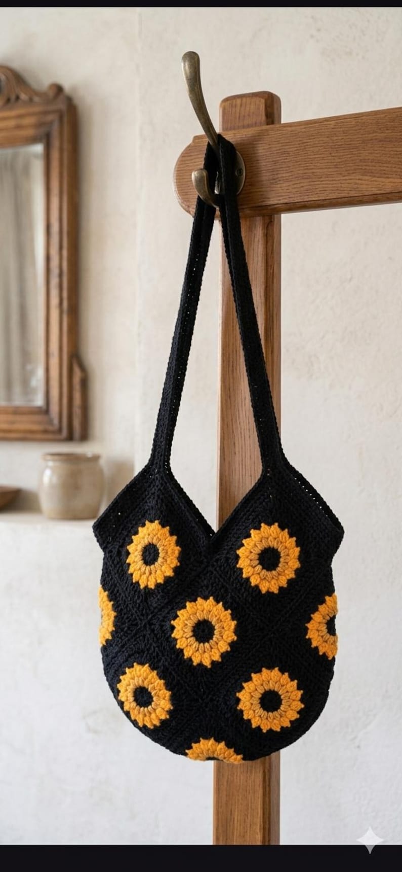 May include: Black crochet tote bag with yellow sunflower appliques. The bag is hanging on a wooden hook. The bag has two long straps and a V-shaped opening. The sunflowers are in full bloom.