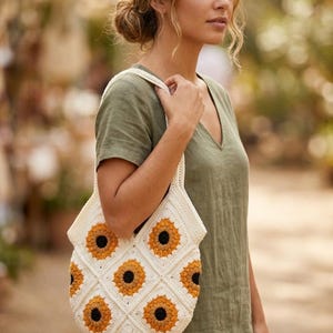 May include: A white crochet tote bag with a sunflower design. The bag features a repeating pattern of yellow and black sunflowers on a white background. The bag has a shoulder strap and is held by a person wearing a green dress.