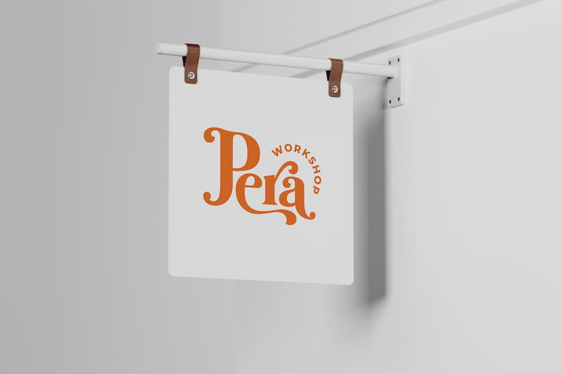 May include: A white square sign with rounded corners hangs from a white metal rod. The sign has a brown logo with the word "Pera" in a stylized font and the word "Workshop" in a smaller font.