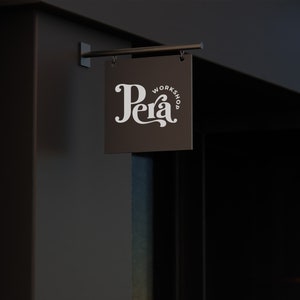 May include: A black sign with white text that reads "Pera Workshop" hanging on a dark brown wall.