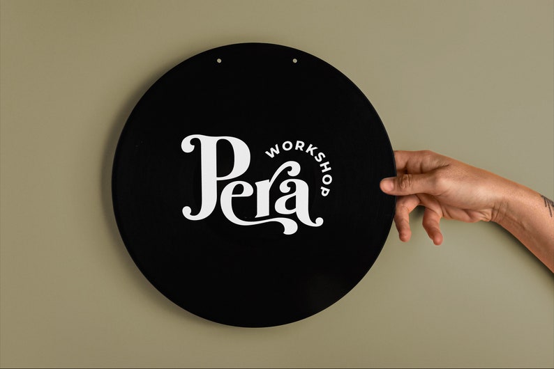 May include: A black circular sign with white text that reads "Pera Workshop". The sign is hanging on a light green wall.