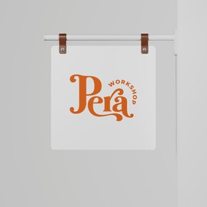 May include: A white sign with brown leather straps hanging from a white metal rod. The sign has the text "Pera Workshop" in orange lettering.