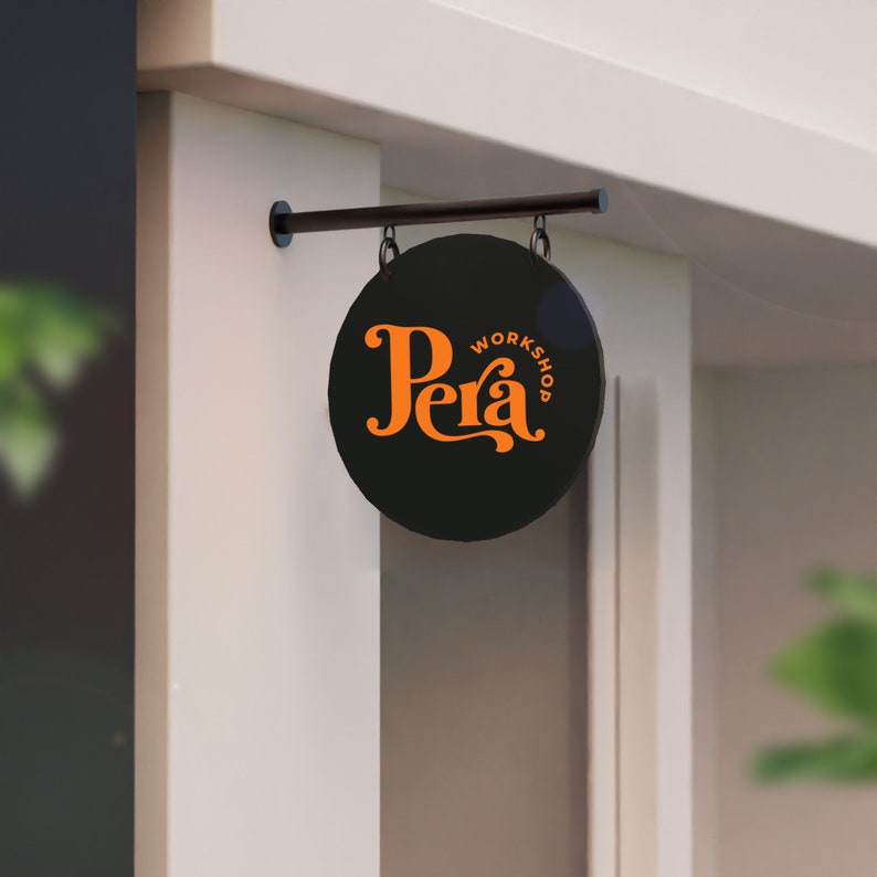 May include: Black and white sign with the text "Pera Workshop" in orange lettering. The sign is hanging from a black metal rod.