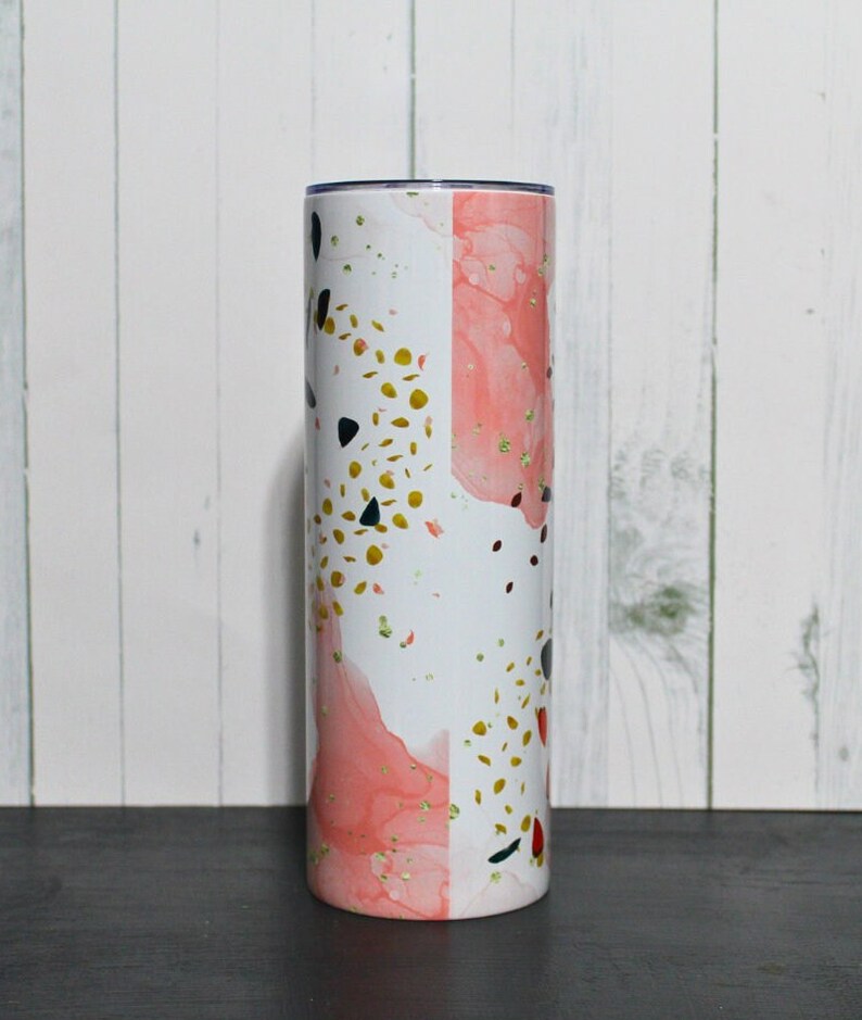 Puede incluir: Un vaso de acero inoxidable blanco y rosa con un dise&ntilde;o abstracto dorado y negro.