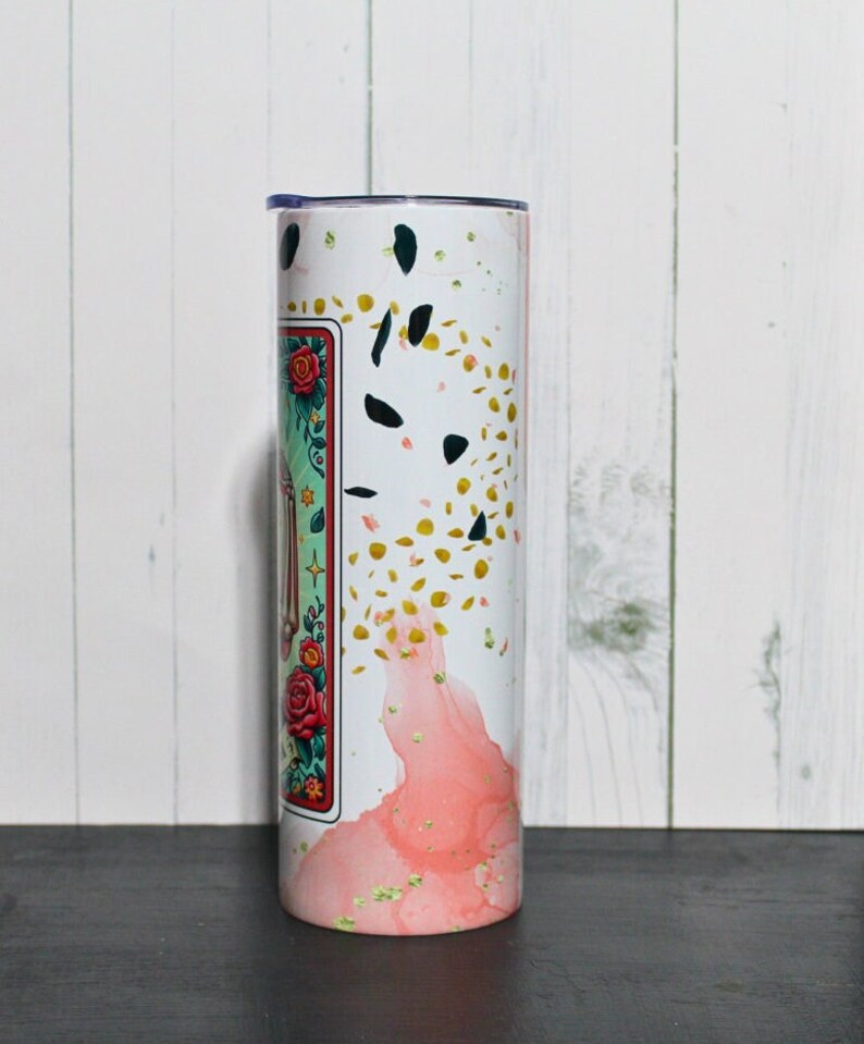 Puede incluir: Un vaso blanco con un dise&ntilde;o rosa y dorado. El dise&ntilde;o presenta un patr&oacute;n floral y purpurina dorada. El vaso tiene una tapa transparente.