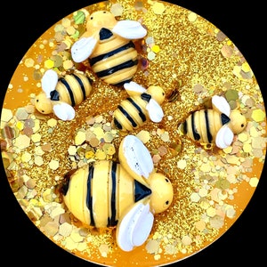 May include: A close-up of a round, yellow, glittery surface with five small, yellow and black bee figurines. The bees have white wings and black eyes.