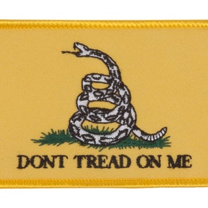 Peut inclure: Un écusson en tissu jaune avec un serpent à sonnettes enroulé et les mots "DONT TREAD ON ME" en noir.