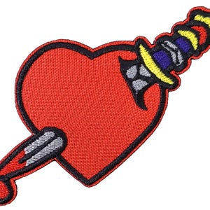 May include: Red heart with a black outline pierced by a yellow, blue, and red dagger with a gray blade. The dagger is dripping red.