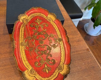 May include: Ornate red and gold decorative tray with a scalloped edge. The tray features a central red panel with gold scrollwork and a gold border. The tray is likely made of wood or a similar material.