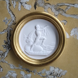 Könnte beinhalten: Eine runde Plakette mit goldenem Rahmen, die eine weiße Keramik-Reliefskulptur einer Figur zeigt, die eine Leier spielt. Die Figur steht auf einem Felsen und ist von Wasser umgeben.