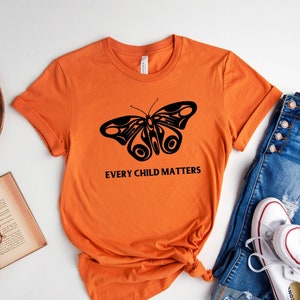 May include: Orange t-shirt with a black butterfly graphic and the text "Every Child Matters".