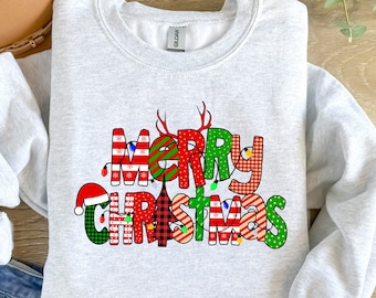 May include: A light gray sweatshirt with the words "MERRY CHRISTMAS" in a colorful, festive design. The letters are decorated with patterns like plaid, stripes, and polka dots, and include Christmas lights and a Santa hat.