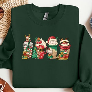 May include: A dark green sweatshirt with a Christmas-themed design featuring five cartoon characters holding cups of coffee or hot chocolate. The characters are dressed in festive attire and include Santa Claus, a reindeer, and a snowman.