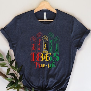 May include: A dark blue t-shirt with a graphic design featuring raised fists with the text "Black History Didn't Start with Slavery" and the year "1865" with the text "Free-ish" below.