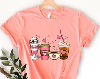Op de afbeelding: Een roze T-shirt met een afbeelding van vier koffiebekers. De bekers zijn versierd met hartjes en de woorden "Mommy" en "Mom".
