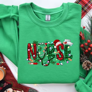May include: Green Christmas themed sweatshirt with the word "NURSE" in red, white, and green plaid with a stethoscope, candy canes, and a Santa hat.