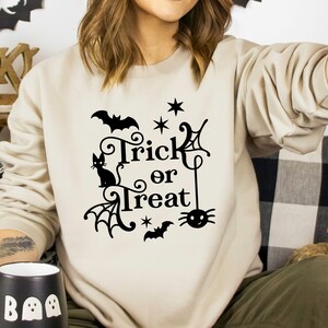 May include: A beige sweatshirt with a black graphic design that says "Trick or Treat" with a black cat, spider, bats, and stars.