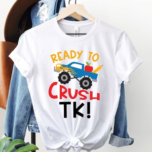 May include: White t-shirt with a blue monster truck graphic and the text "Ready to Crush TK!" in red and yellow letters.
