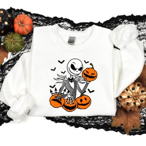 May include: White sweatshirt with a black and white illustration of Jack Skellington from The Nightmare Before Christmas holding a pumpkin. The illustration includes bats flying around Jack Skellington.
