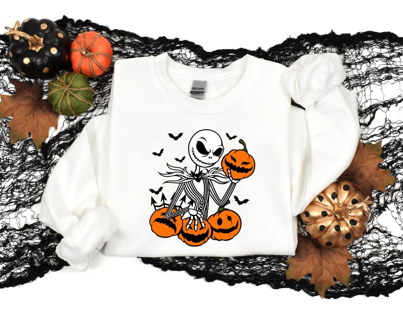 May include: White sweatshirt with a black and white illustration of Jack Skellington from The Nightmare Before Christmas holding a pumpkin. The illustration includes bats flying around Jack Skellington.