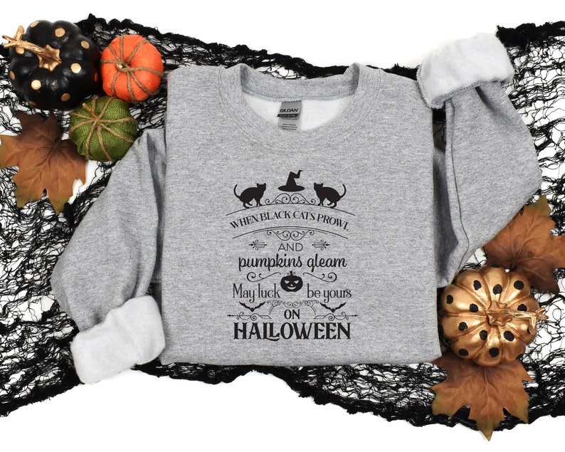 Peut inclure: Sweat-shirt gris avec un imprim&eacute; graphique noir qui dit "When black cats prowl and pumpkins gleam may luck be yours on HALLOWEEN". Le graphique comprend &eacute;galement un chat noir, un chapeau de sorci&egrave;re et une citrouille.