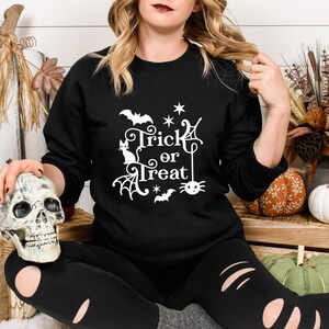 May include: A black sweatshirt with a white graphic design that says "Trick or Treat" with a cat, spider, and bats.
