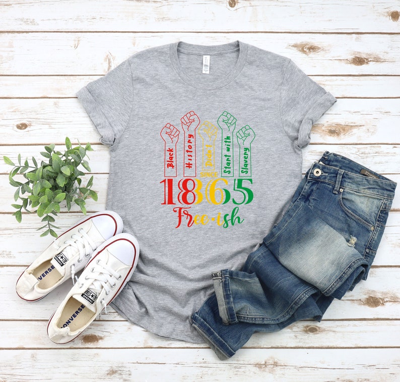 May include: Gray t-shirt with a graphic design of five raised fists with text that reads "Black History", "Stand with Slavery", and "1865 Free-ish".