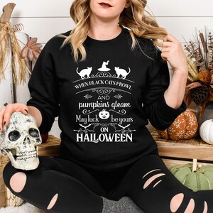 Peut inclure: Un sweat-shirt noir avec un motif graphique blanc qui dit "When black cats prowl and pumpkins gleam, may luck be yours on Halloween". Le graphique comprend &eacute;galement deux chats noirs et une citrouille.