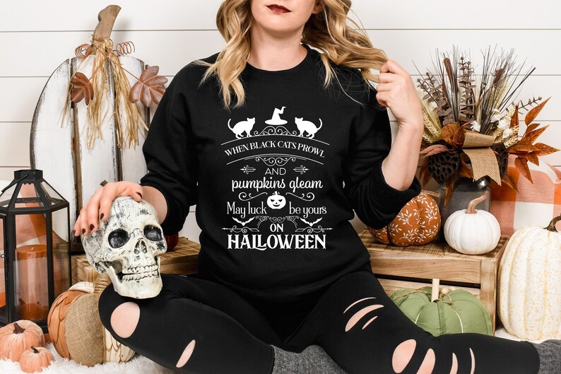 Peut inclure: Un sweat-shirt noir avec un motif graphique blanc qui dit "When black cats prowl and pumpkins gleam, may luck be yours on Halloween". Le graphique comprend &eacute;galement deux chats noirs et une citrouille.
