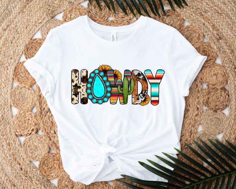 K&ouml;nnte beinhalten: Wei&szlig;es T-Shirt mit dem Wort "HOWDY" in bunten Buchstaben. Die Buchstaben sind mit s&uuml;dwestlichen Mustern verziert, darunter t&uuml;rkisfarbene Steine, Kakteen und Sonnenblumen.