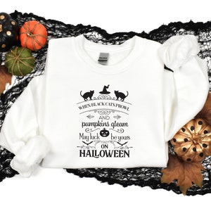 Peut inclure: Sweat-shirt blanc avec un imprim&eacute; graphique noir qui dit "When black cats prowl and pumpkins gleam may luck be yours on Halloween". Le graphique comprend &eacute;galement deux chats noirs et une citrouille.