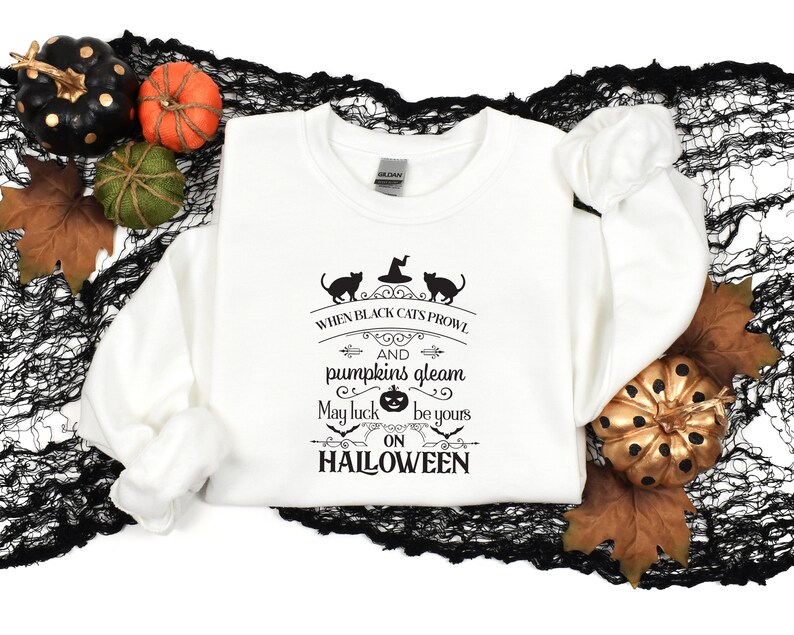 Peut inclure: Sweat-shirt blanc avec un imprim&eacute; graphique noir qui dit "When black cats prowl and pumpkins gleam may luck be yours on Halloween". Le graphique comprend &eacute;galement deux chats noirs et une citrouille.