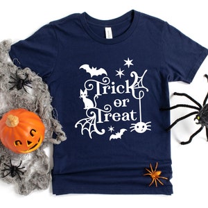 May include: A navy blue t-shirt with a white graphic design that says "Trick or Treat" with a spider, bat, and cat. The design is surrounded by stars and spiderwebs.
