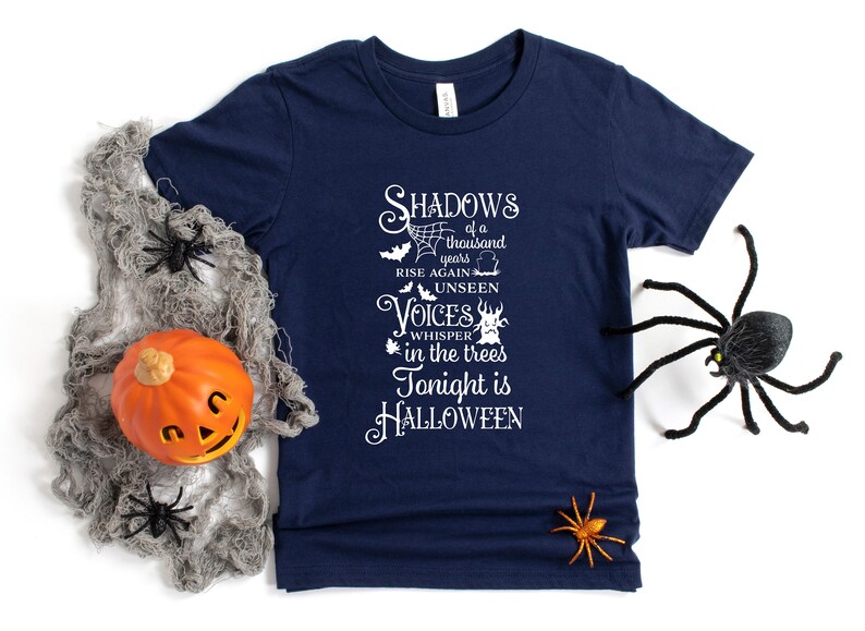 K&ouml;nnte beinhalten: Ein marineblaues T-Shirt mit einer wei&szlig;en Grafik, auf der steht "Shadows of a thousand years rise again unseen voices whisper in the trees tonight is HALLOWEEN".