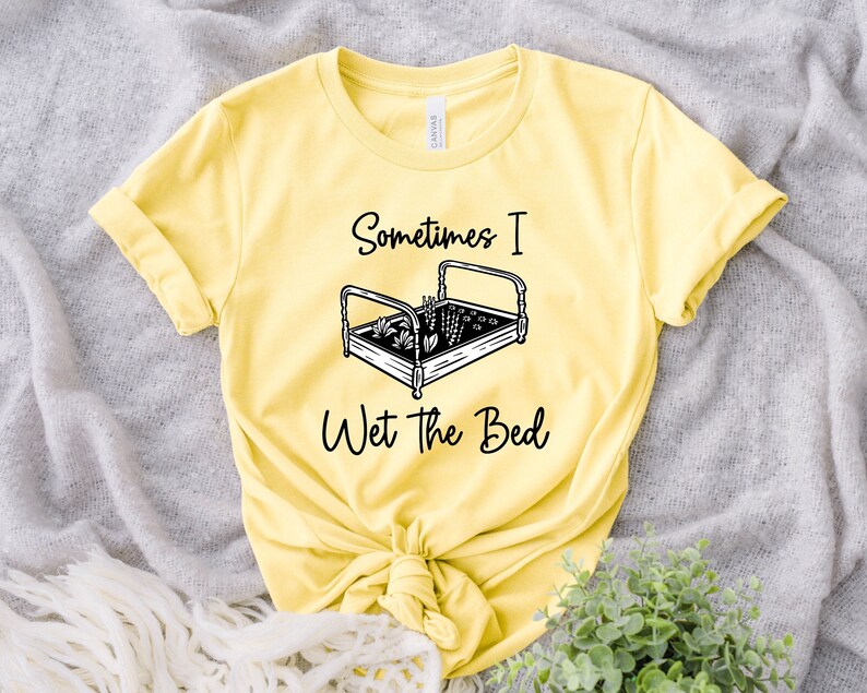 K&ouml;nnte beinhalten: Gelbes T-Shirt mit einer schwarz-wei&szlig;en Grafik eines Bettes mit darin wachsenden Pflanzen. Der Text "Sometimes I Wet the Bed" ist unter der Grafik aufgedruckt.