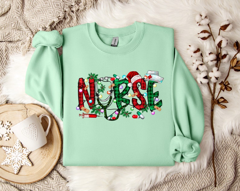 May include: A light green sweatshirt with a Christmas-themed design that says "NURSE" in red and green plaid with a stethoscope, a syringe, and other medical symbols.