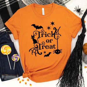 May include: Orange t-shirt with a black graphic that says "Trick or Treat" with a black cat, bats, and a spider.